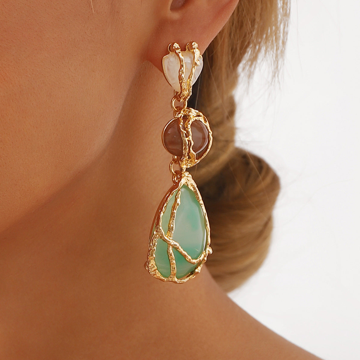 Gold earring with a green teardrop-shaped gemstone worn by a person.