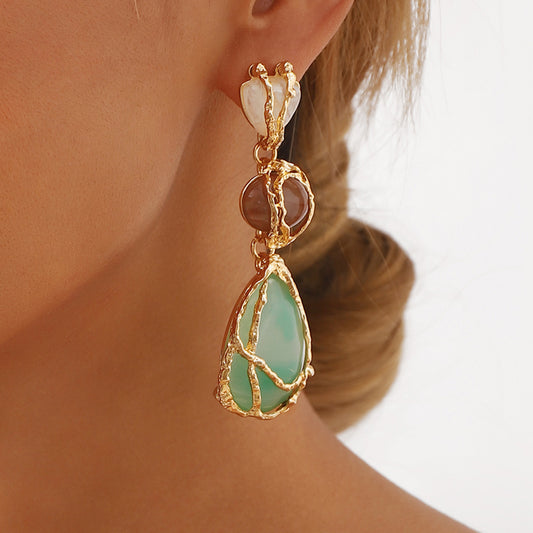 Gold earring with a green teardrop-shaped gemstone worn by a person.